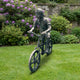Life-Size Contemporary Boy on BMX Bicycle Bronze Sculpture by Giant Sculptures, antique brown-green patina, shown on a lawn beside pink rhododendrons.