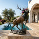 Life-Size Contemporary Bugling Elk Bronze Sculpture by Giant Sculptures, head raised mid-bugle with foreleg lifted on a rocky base, displayed poolside by a villa.