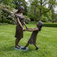 Life-Size Contemporary Children Bronze Statue from Giant Sculptures showing a taller girl and smaller girl holding hands and leaning back mid-spin on a garden lawn.