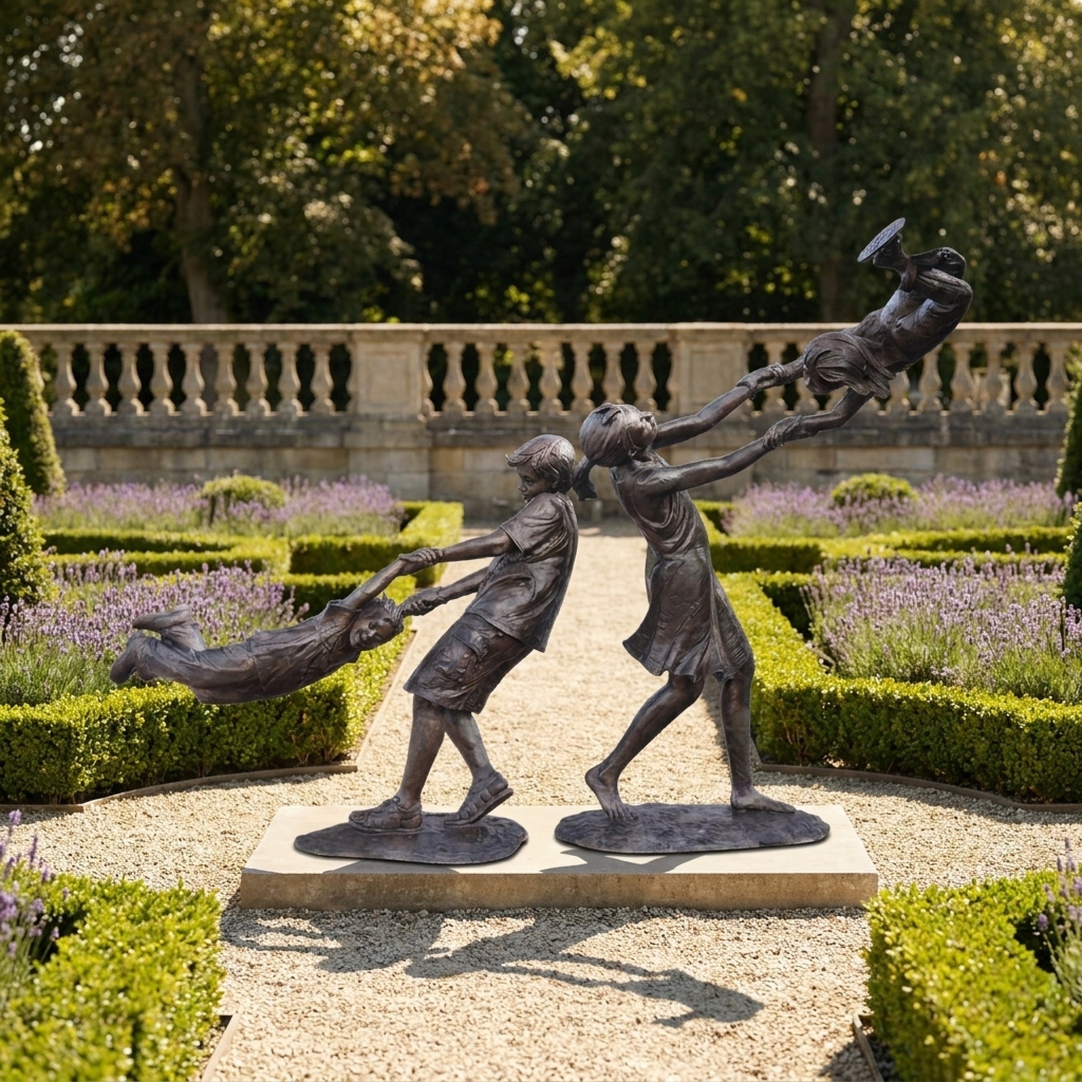 Life-Size Contemporary Children Playing Bronze Sculpture by Giant Sculptures, warm brown patina, displayed on a gravel path in a formal lavender garden.