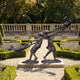 Life-Size Contemporary Children Playing Bronze Sculpture by Giant Sculptures, warm brown patina, displayed on a gravel path in a formal lavender garden.