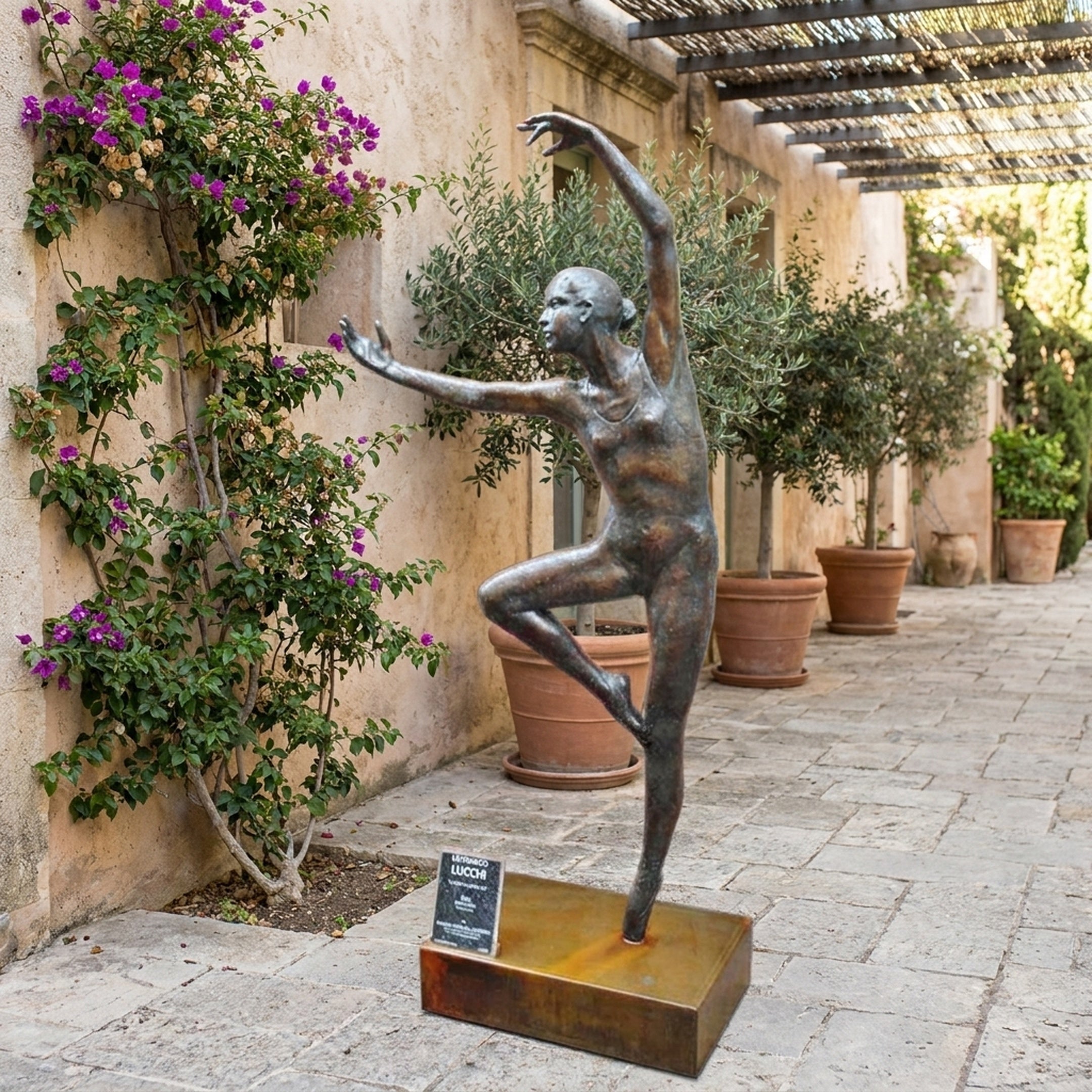 Life-Size Contemporary Female Dancer Bronze Sculpture by Giant Sculptures in arabesque pose on a bronze plinth, displayed in a stone courtyard with bougainvillea.