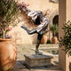 Giant Sculptures Life-Size Female Figure Skater Bronze Sculpture on a stone plinth in a sunlit Mediterranean courtyard beside a pool and potted olive trees.