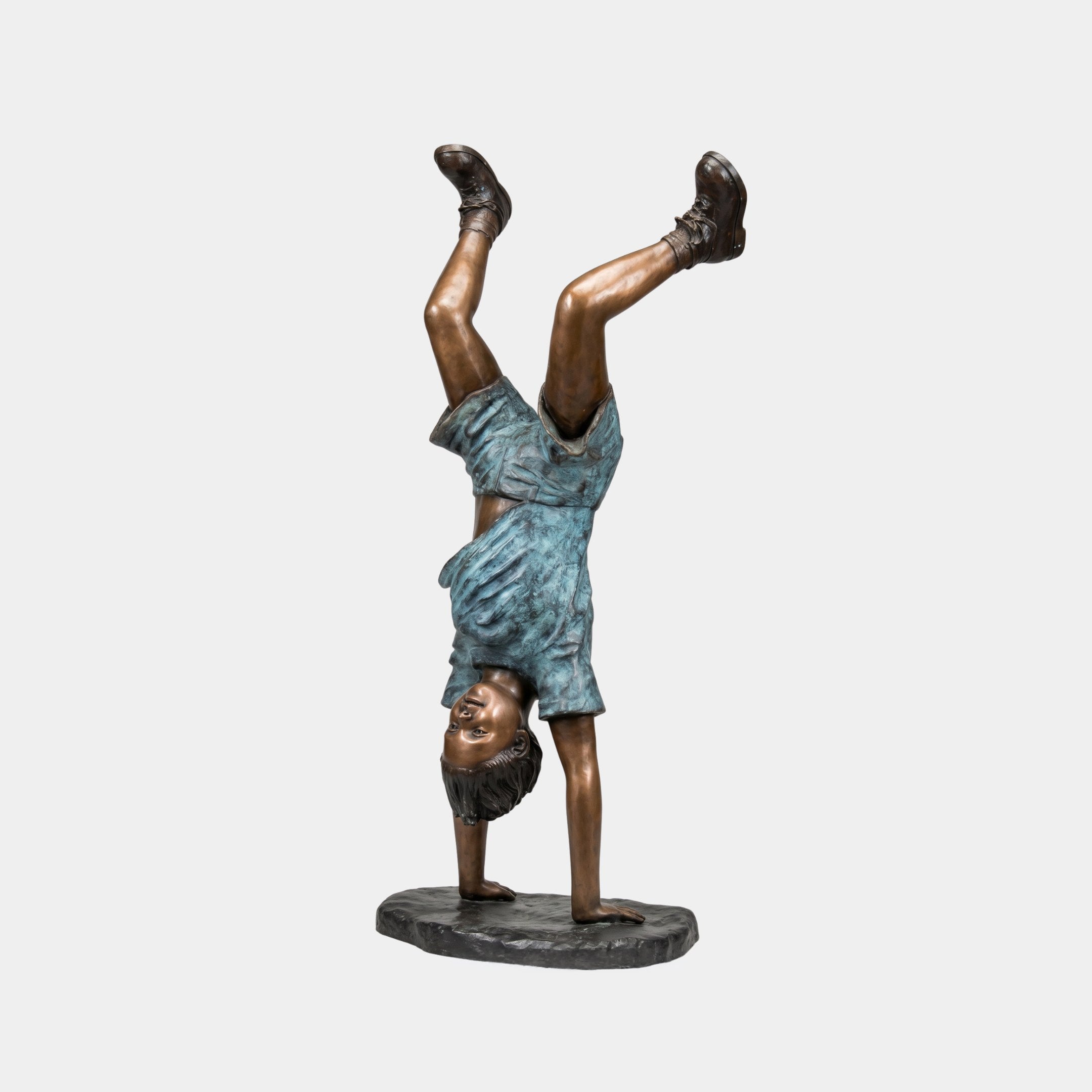Life-Size Contemporary Handstand Child Bronze Sculpture by Giant Sculptures, showing a smiling child in a blue verdigris dress balancing on hands, on a flat base.