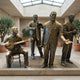 Life-Size Contemporary Jazz Band Bronze Sculpture from Giant Sculptures, showing four patinated musicians with banjo, trombone, vocalist, and wind instrument in a sunlit atrium.
