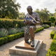 Life-Size Contemporary Kneeling Soldier Bronze Statue by Giant Sculptures, 150cm, cradling a folded flag with gold stars, displayed in a lavender garden path.