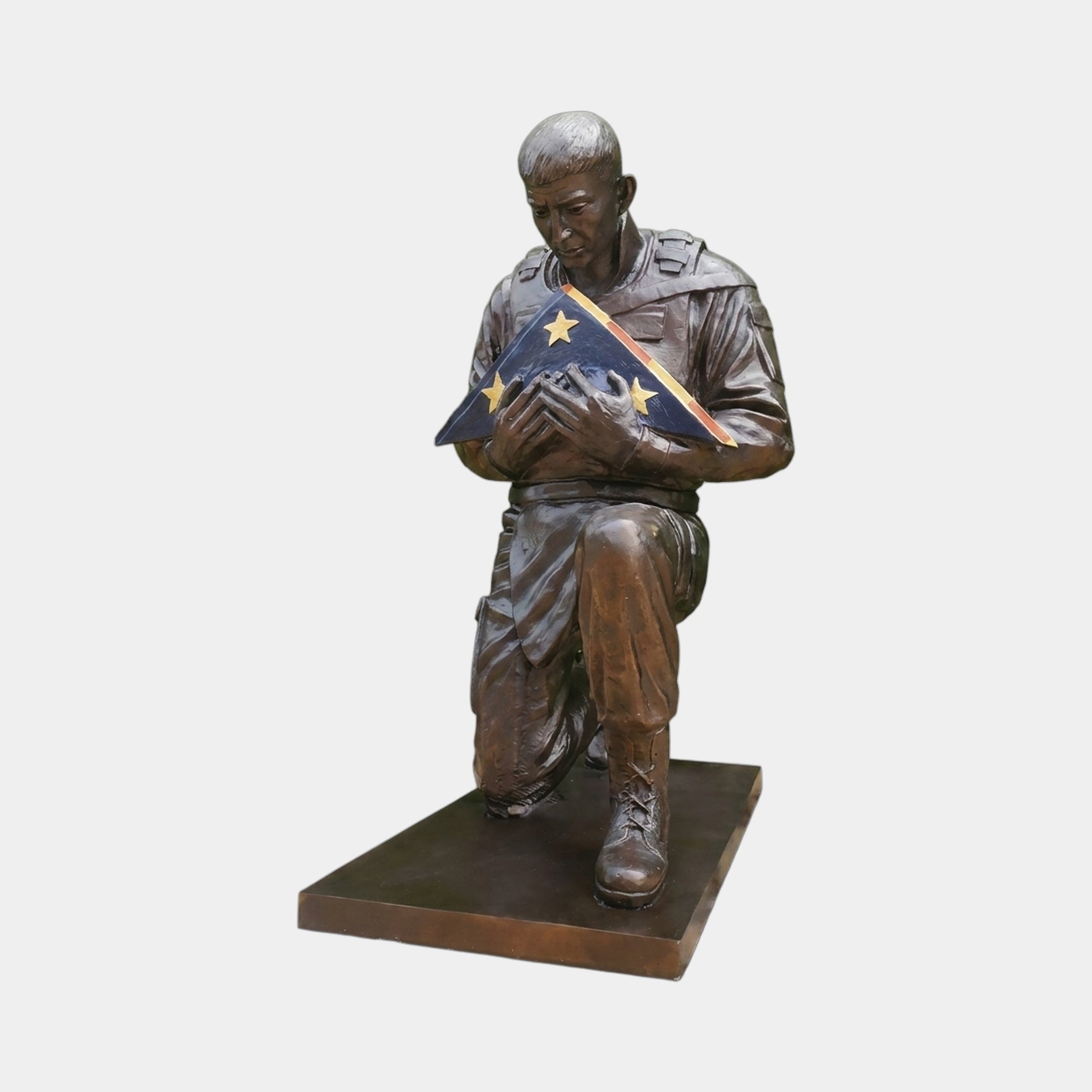 Life-Size Contemporary Kneeling Soldier Bronze Statue by Giant Sculptures, 150cm, kneeling figure cradling a folded flag with gold stars, on a plain background.