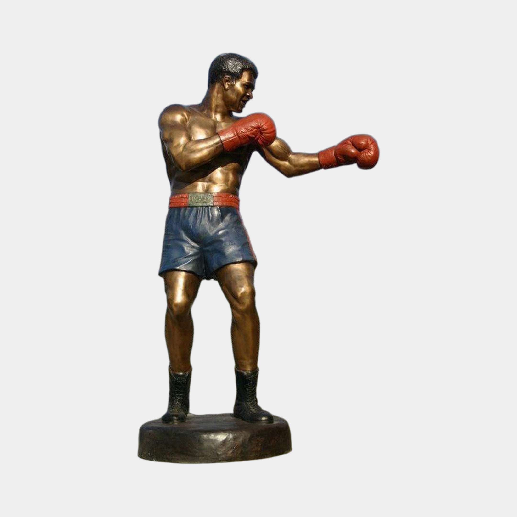Life-Size Contemporary Male Boxer Bronze Sculpture by Giant Sculptures, shown mid-jab in red gloves and blue shorts on an oval base against a light background.