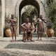 Life-Size Contemporary Musician Trio Bronze Sculpture by Giant Sculptures, flutist, seated guitarist and violinist in warm patina, set on gravel by a stone archway.