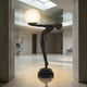 Life-Size Contemporary Nude Female Figure Bronze Sculpture 210cm by Giant Sculptures, leaning forward to hold a glowing frosted globe lamp in a gallery interior.