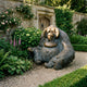 Life-Size Contemporary Orangutan Bronze Bust by Giant Sculptures seated on a gravel path in a walled garden with roses, foxgloves, and a wooden door behind.