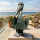Life-Size Contemporary Pelican Bronze Sculpture by Giant Sculptures with verdigris patina and waistcoat detail, displayed on a stone base on a beachside terrace.