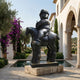 Life-Size Contemporary Rotund Rider and Horse Bronze Sculpture by Giant Sculptures on a pale stone plinth in a Mediterranean courtyard with bougainvillea.