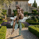 Life-Size Contemporary Seated Female Figure Bronze Sculpture by Giant Sculptures on a verdigris lotus stem in a formal Tuscan villa garden with lavender.