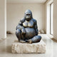 Life-Size Contemporary Seated Gorilla Bronze Sculpture by Giant Sculptures, 250cm, with dark patina and golden-brown chest, displayed on a stone slab in a minimalist room.