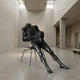 Giant Sculptures Life-Size Contemporary Seated Male Figure Bronze Sculpture 150cm in matte black, reclining on a slender metal chair in a pale gallery.
