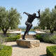 Giant Sculptures Life-Size Sprinting Male Figure Bronze Sculpture in dark patina on a stone block, mid-stride with arms flung wide, beside a pool and olive trees.