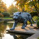 Life-Size Contemporary Stalking Tiger Bronze Sculpture by Giant Sculptures in blue-grey patina, mid-roar on stone paving beside a garden pond at sunset.