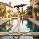 Life-Size Contemporary Walking Woman Bronze Fountain by Giant Sculptures, 190cm golden-brown figure mid-stride holding a lotus leaf canopy beside a poolside terrace.