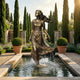 Life-Size Contemporary Walking Woman Bronze Fountain by Giant Sculptures, 220cm figure mid-stride with flowing dress above a rectangular pond in a cypress garden.