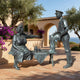Life-Size Conversing Couple on Bench Bronze Sculpture by Giant Sculptures with green-grey patina, displayed on a terracotta terrace with olive tree and bougainvillea.