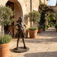 Life-Size Defiant Girl Bronze Sculpture by Giant Sculptures, 130cm, standing hands on hips on a cobblestone base in a Mediterranean stone courtyard.