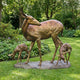 Life-Size Doe and Fawns Bronze Sculpture by Giant Sculptures, showing a standing doe with two grazing spotted fawns on a stone-effect base in a garden.