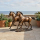 Life-Size Galloping Horse Pair Bronze Sculpture by Giant Sculptures shown on a seaside stone terrace beside terracotta planters of succulents, with ocean behind.
