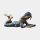 Life-Size Girl Reading Book Bronze Sculpture by Giant Sculptures, shown lying prone with bare feet raised and head bent over an open book, on a plain background.