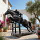 Life-Size Jockey and Horse Clearing a Jump Bronze Sculpture by Giant Sculptures on a Mediterranean terrace with olive trees, bougainvillea, and sea view.