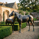 Life-Size Mare and Foal Bronze Sculpture by Giant Sculptures, dark patinated mare turning toward the foal at her side, displayed on gravel beside a walled garden.