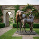 Life-Size Mare and Foal with Female Handler Bronze Sculpture by Giant Sculptures, dark brown patina, displayed in a walled rose garden near an arched gateway.