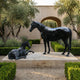Life-Size Mare and Reclining Foal Bronze Sculpture by Giant Sculptures on a stone plinth in a courtyard with olive trees, lavender, and boxwood hedges.