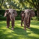 Life-Size Pair of African Elephants Bronze Sculpture by Giant Sculptures shown frontally on a sunlit lawn, with reddish-brown patina, flared ears, and lowered trunks.