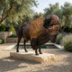 Life-Size Standing Bison Bull Bronze Sculpture by Giant Sculptures, 220cm, on a stone plinth beside a sunken pool in an olive and lavender garden.