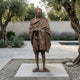 Life-Size Standing Gandhi Figure Bronze Statue by Giant Sculptures, 180cm, displayed on a stone plinth in a garden courtyard with olive trees and lavender.