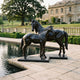 Life-Size Standing Mare and Foal Bronze Sculpture by Giant Sculptures in deep black patina, displayed on stone paving beside a reflecting pool at a manor estate.