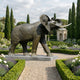 Life-Size Traditional African Elephant Bronze Sculpture by Giant Sculptures with raised trunk and ivory tusks, on a granite plinth in a formal cypress garden.