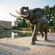 Life-Size Traditional African Elephant Bronze Sculpture by Giant Sculptures, trunk raised in trumpeting pose, displayed beside a reflecting pool at a château.