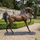 Life-Size Traditional Arabian Horse Bronze Sculpture by Giant Sculptures, foreleg raised in mid-stride with two-tone brown and black patina, set on a gravel garden path.