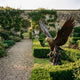 Life-Size Traditional Bald Eagle Bronze Sculpture by Giant Sculptures with wings raised, set on grass beside a gravel path in a walled garden with box hedges.