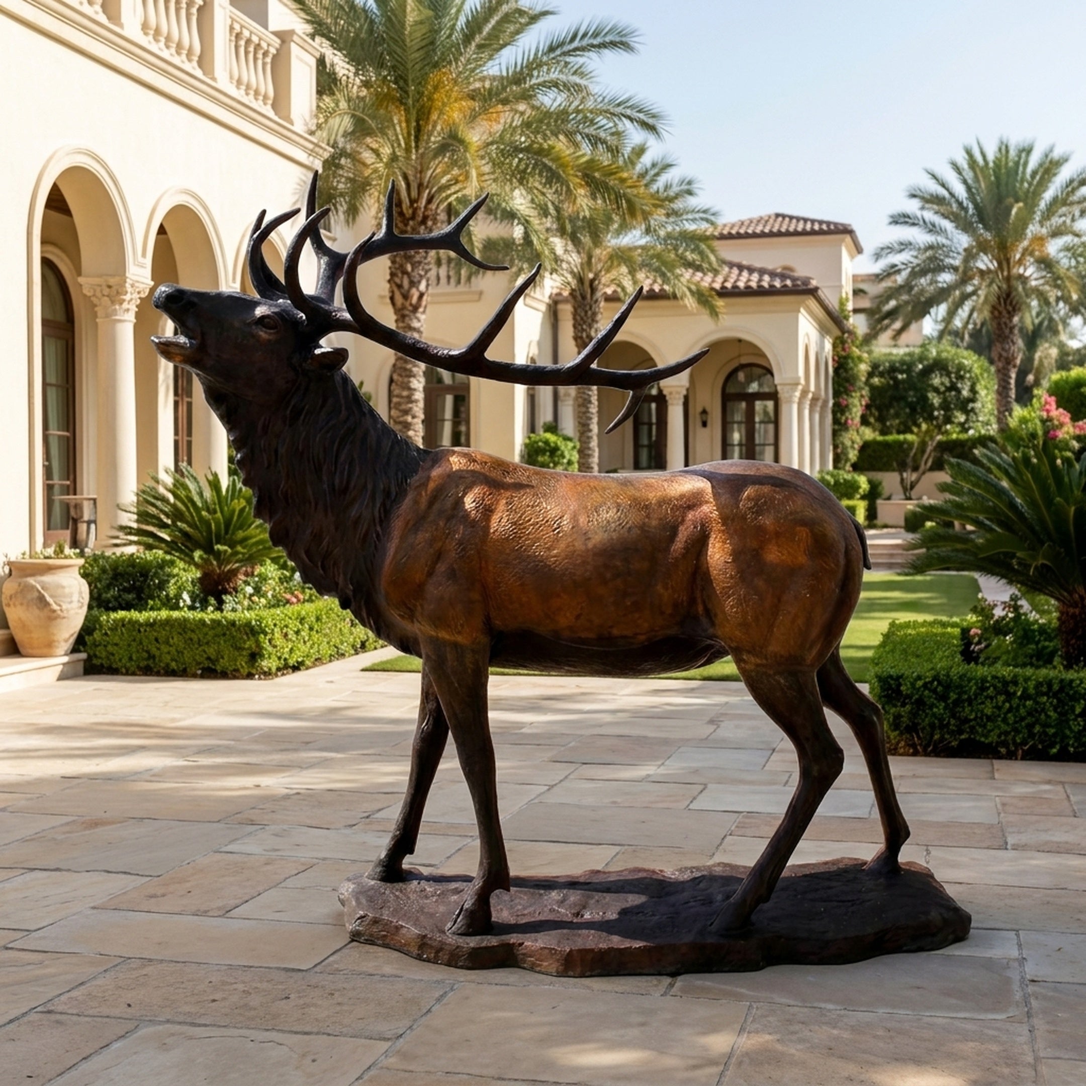 Life-Size Traditional Bugling Bull Elk Bronze Sculpture by Giant Sculptures shown mid-bugle on a rocky base in a Mediterranean villa courtyard with palms.