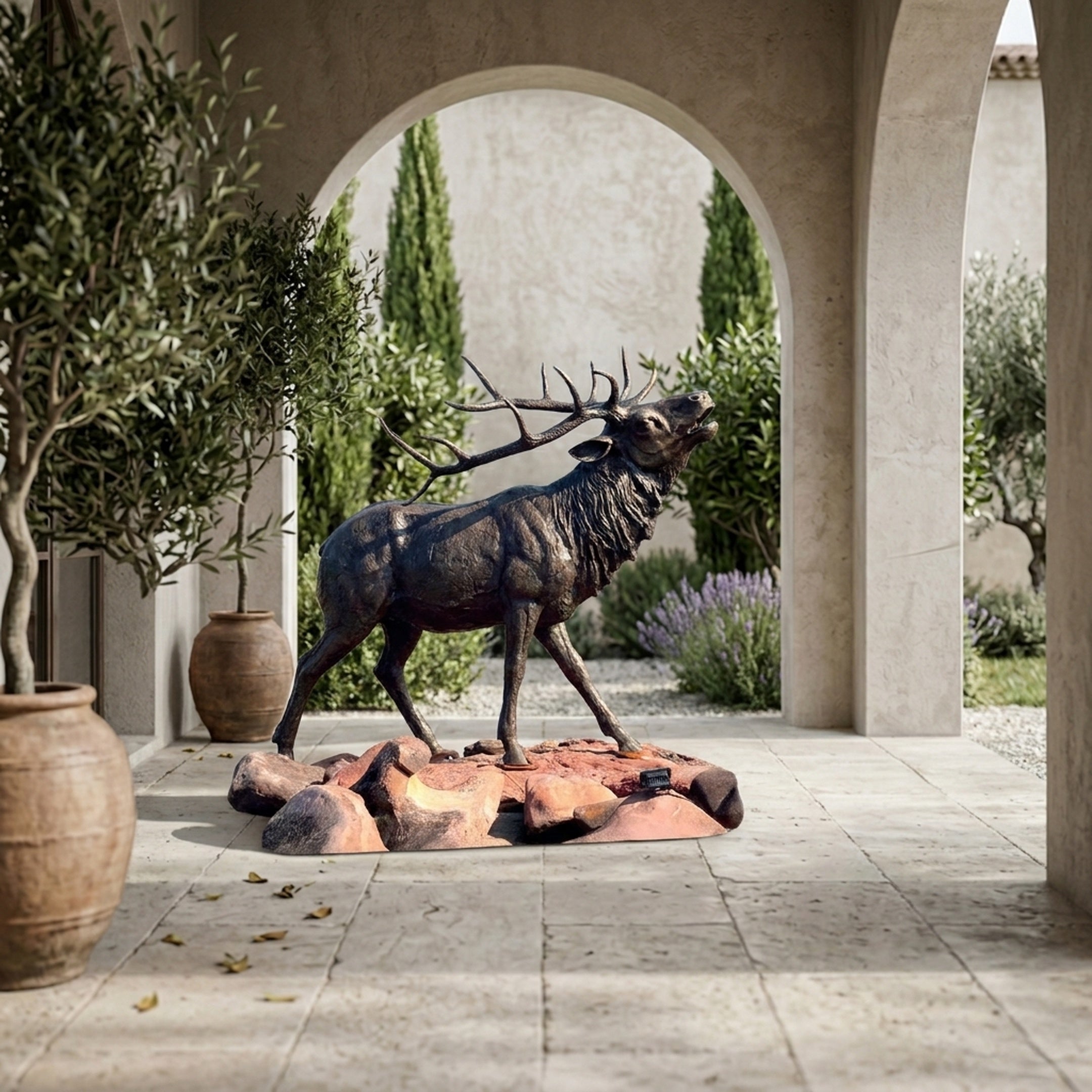 Life-Size Traditional Bugling Elk Bronze Sculpture by Giant Sculptures on a boulder base, displayed under a stucco archway with olive trees and cypress.
