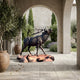 Life-Size Traditional Bugling Elk Bronze Sculpture by Giant Sculptures on a boulder base, displayed under a stucco archway with olive trees and cypress.