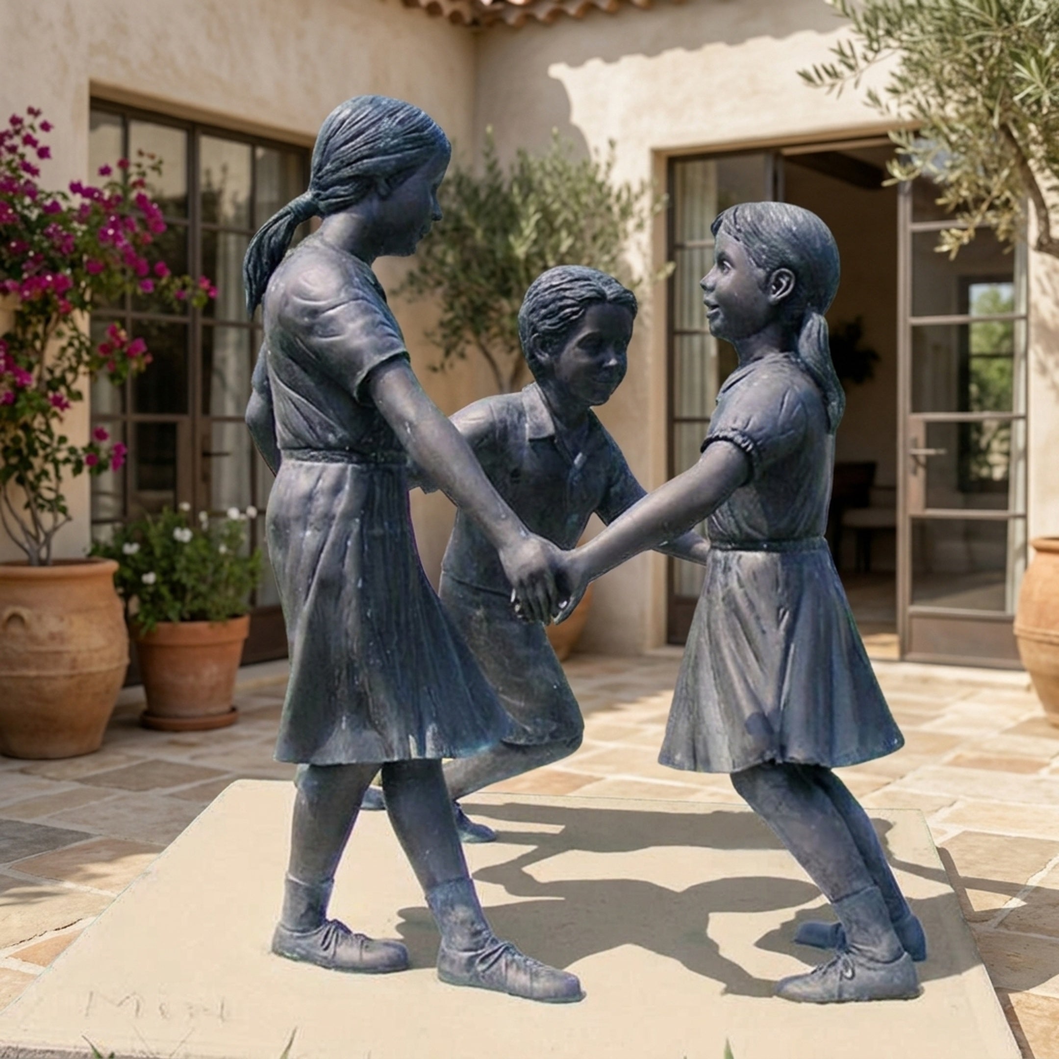 Life-Size Traditional Children Playing Bronze Sculpture by Giant Sculptures, three children clasping hands in a ring, displayed on a sunlit Mediterranean courtyard.