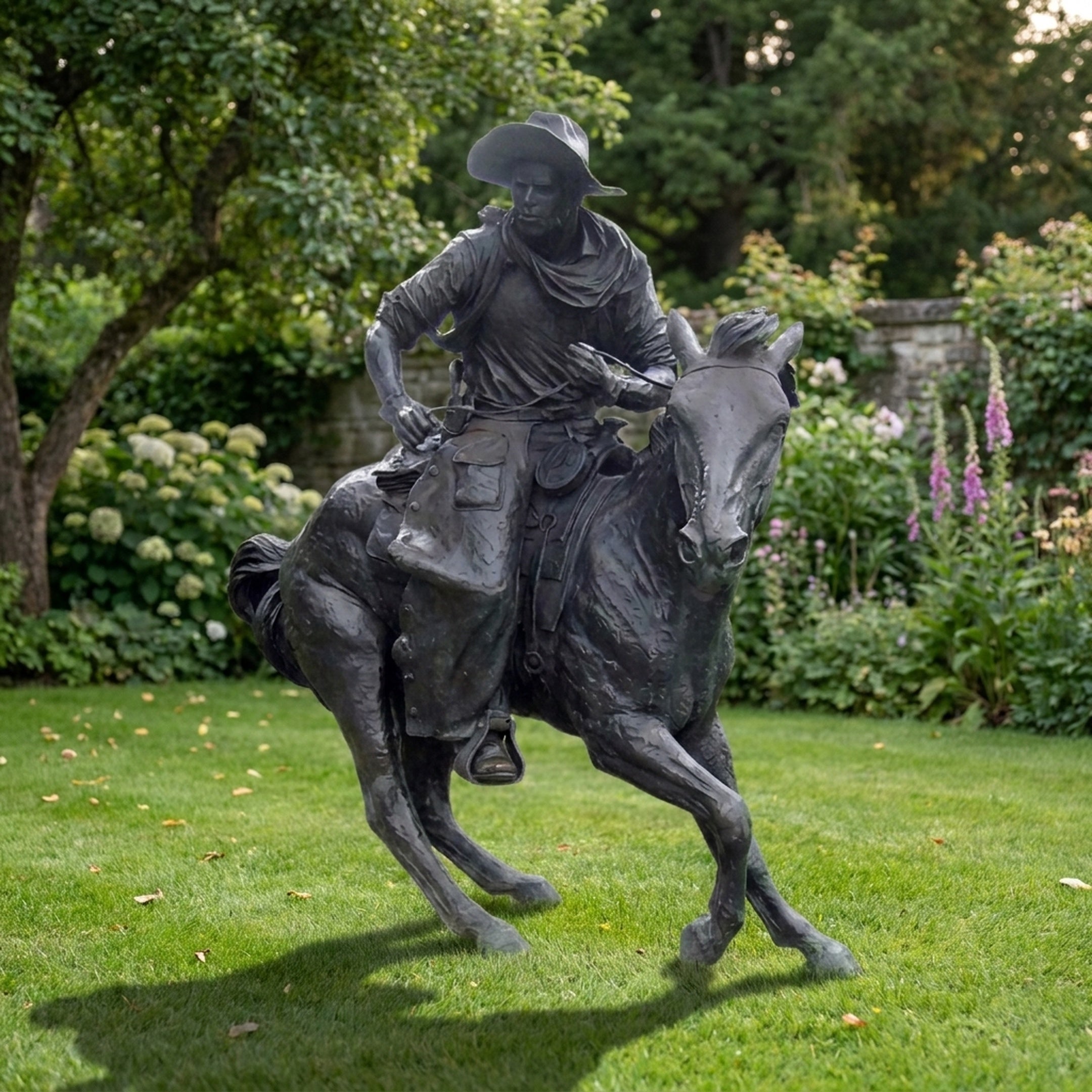 Life-Size Traditional Cowboy Riding Galloping Horse Bronze Sculpture by Giant Sculptures, dark patina, displayed on a lawn beside hydrangeas and foxgloves.