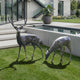 Life-Size Traditional Deer Bronze Sculpture Pair by Giant Sculptures, with an antlered stag standing alert beside a grazing doe on lawn by a modern concrete home.