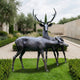 Life-Size Traditional Deer Pair Bronze Sculpture by Giant Sculptures showing an antlered stag standing alert behind a grazing doe on a manicured garden lawn.