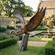 Life-Size Traditional Eagle Bronze Sculpture by Giant Sculptures, wings raised and talons clutching a coiled serpent, displayed in a formal garden by a pond.
