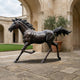 Life-Size Traditional Galloping Horse Bronze Sculpture by Giant Sculptures with dark patina, shown mid-stride in a stone courtyard beside an arched colonnade.